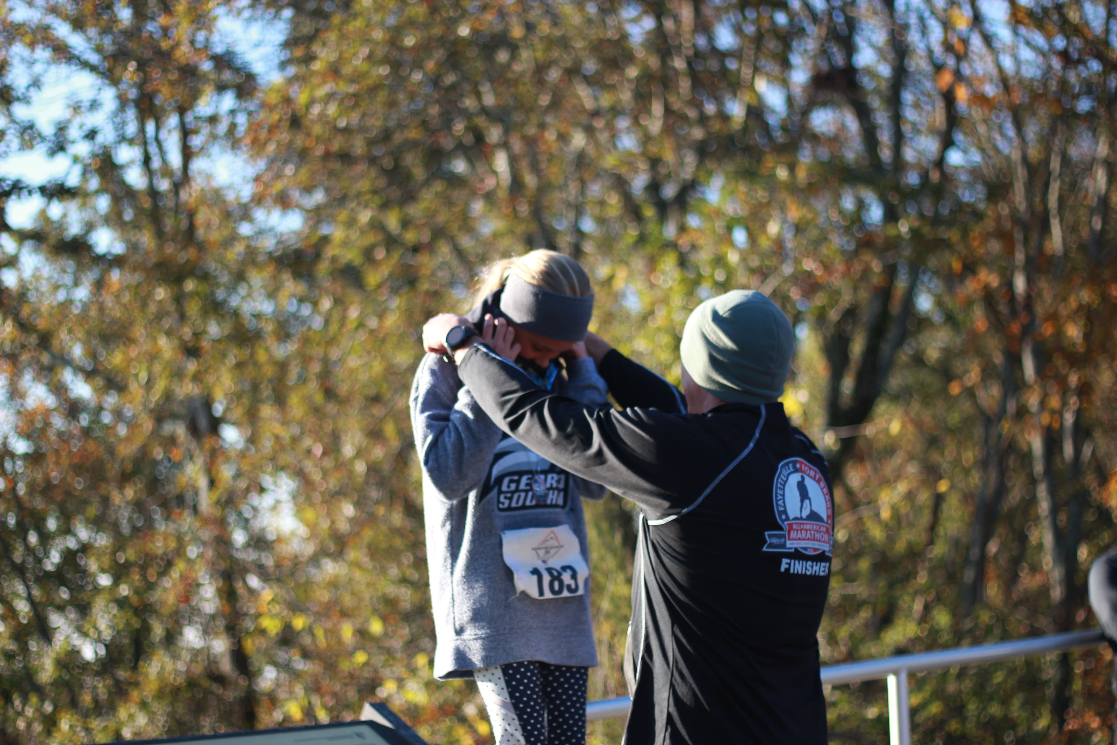Adult placing a finisher medal on a young runner after the race